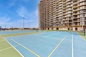 Ein Tennisplatz im Freien neben einem Hochhaus mit mehreren Balkonen.
