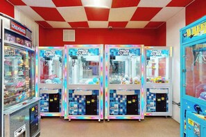 Eine Reihe von Prize Cube-Greifautomaten in einer hell erleuchteten Spielhalle mit rot-weiß karierter Decke.