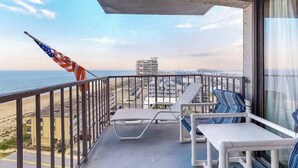 Ein Balkon mit zwei Liegestühlen, einer Flagge und Blick auf Strand und Meer.
