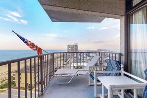 Ein Balkon mit zwei Liegestühlen, einer Flagge und Blick auf Strand und Meer.