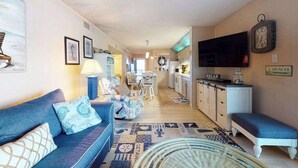 Ein Wohnzimmer mit einer Couch, einem Essbereich, einer Küche und einem Fernseher.