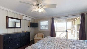 Ein Schlafzimmer mit Bett, Schminktisch, Fernseher, Stuhl und einem Balkon mit Vorhängen.