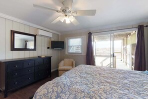 Ein Schlafzimmer mit Bett, Schminktisch, Fernseher, Stuhl und einem Balkon mit Vorhängen.