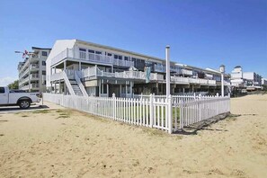 Ein mehrstöckiges Hotel mit Balkonen, einem weißen Zaun und blauem Himmel.