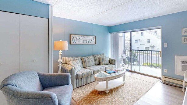 A living room with a sofa, armchair, coffee table, and a sign that reads 'Sandy Feet Welcome.' - Sea Place 108 (Ocean City)