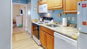 A kitchen with wooden cabinets, a microwave, stove, sink, and a refrigerator. - Sea Place 108 (Ocean City)