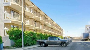 A multi-story residential building with balconies, parked vehicles, and a clear sky. - Sea Place 108 (Ocean City)