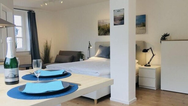 Habitación de hotel con cama, mesitas de noche, escritorio con silla, una botella de champán y una copa.