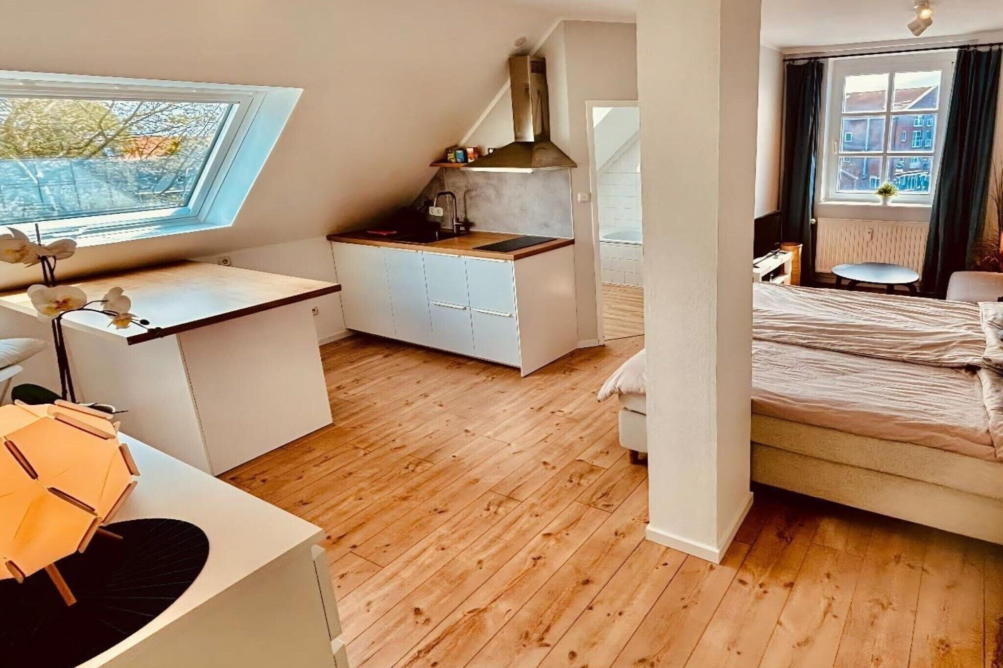A modern bedroom with a wooden floor, a bed, a desk, and a window.