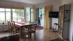 Un área de comedor con una mesa y sillas, un televisor en la pared y vistas al exterior.