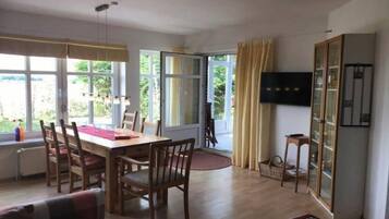 Ein Essbereich mit Tisch und Stühlen, einem Fernseher an der Wand und Blick ins Freie.