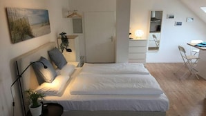 Un dormitorio con cama, mesita de noche, lámpara y una planta.