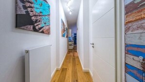 Un corridoio con pavimento in legno, pareti bianche e una porta con rivestimento esterno blu e bianco.