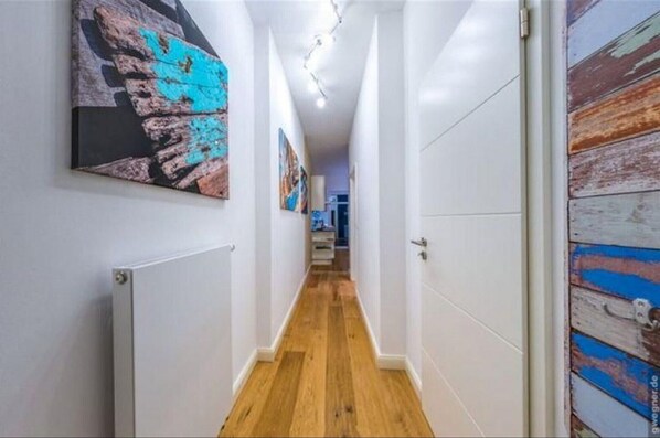 Passadís amb sòl de fusta, parets blanques i una porta amb exterior pintat de blau i blanc.