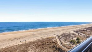 Vista sulla spiaggia con cielo sereno, spiaggia sabbiosa e una recinzione parallela alla riva.