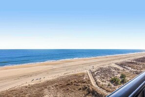Blick auf einen Strand mit klarem Himmel, sandigem Ufer und einer parallel zum Strand verlaufenden Umzäunung.