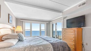 Una camera da letto con un letto, una cassettiera, una TV e ampie finestre con vista.