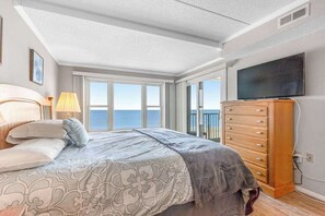 Ein Schlafzimmer mit Bett, Kommode, Fernseher und großen Fenstern mit Blick.