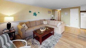 A living room with a beige sofa, a glass coffee table, and a striped armchair. - Newly updated condo - less than a block to the beach (Ocean City)
