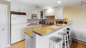 A kitchen with white cabinets, a microwave, a refrigerator, a coffee maker, and a bar stool. - Newly updated condo - less than a block to the beach (Ocean City)