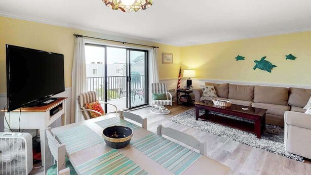 A living room with a TV, sofa, dining table, and a balcony with sliding doors. - Newly updated condo - less than a block to the beach (Ocean City)