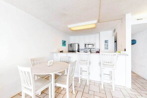 Une cuisine compacte avec des meubles blancs, un îlot central doté de sièges et une petite table à manger.