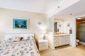 Un dormitorio con cama, mesita de noche y baño con lavamanos y espejo.