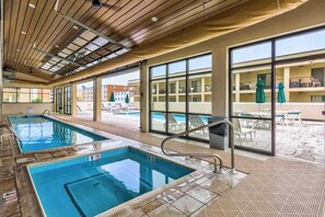 An indoor swimming pool with clear glass walls, a wooden ceiling, and a view of the outside buildings. - Royal Hawaiian 211 (Ocean City)
