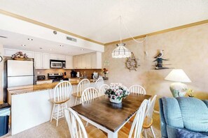 Una cocina moderna con armarios blancos, una isla de madera y un comedor con mesa de madera y sillas blancas.