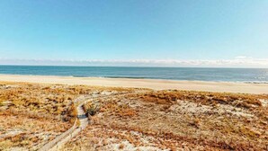 A beach with a sandy path leading to the water, a clear sky, and distant mountains. - Oceanfront Condo w/ Great Beach View, Balcony, AC, W/D & Shared Pool/Tennis (Ocean City)