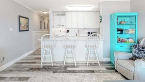 A modern kitchen with white cabinets, a central island, and three white bar stools. - Oceanfront Condo w/ Great Beach View, Balcony, AC, W/D & Shared Pool/Tennis (Ocean City)