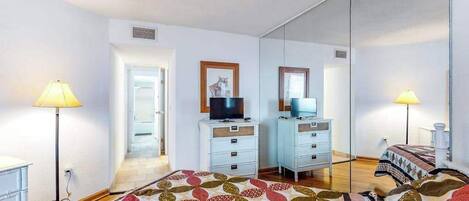 A bedroom with a bed, two bedside tables, a television, a mirror, and a door leading to another room.