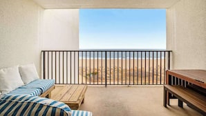 Un balcón con vista a la playa, un banco de madera y un sofá a rayas.