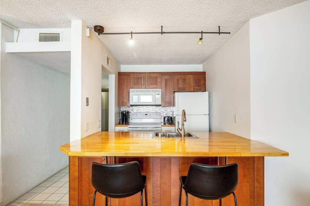 A kitchen with wooden cabinets, a stainless steel refrigerator, and a wooden island with two black chairs.