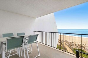 A balcony with a table and chairs, a view of the beach, and a clear sky. - Oceanfront Condo with a Balcony, AC, WiFi, Ocean View & Shared Outdoor Pool (Ocean City)