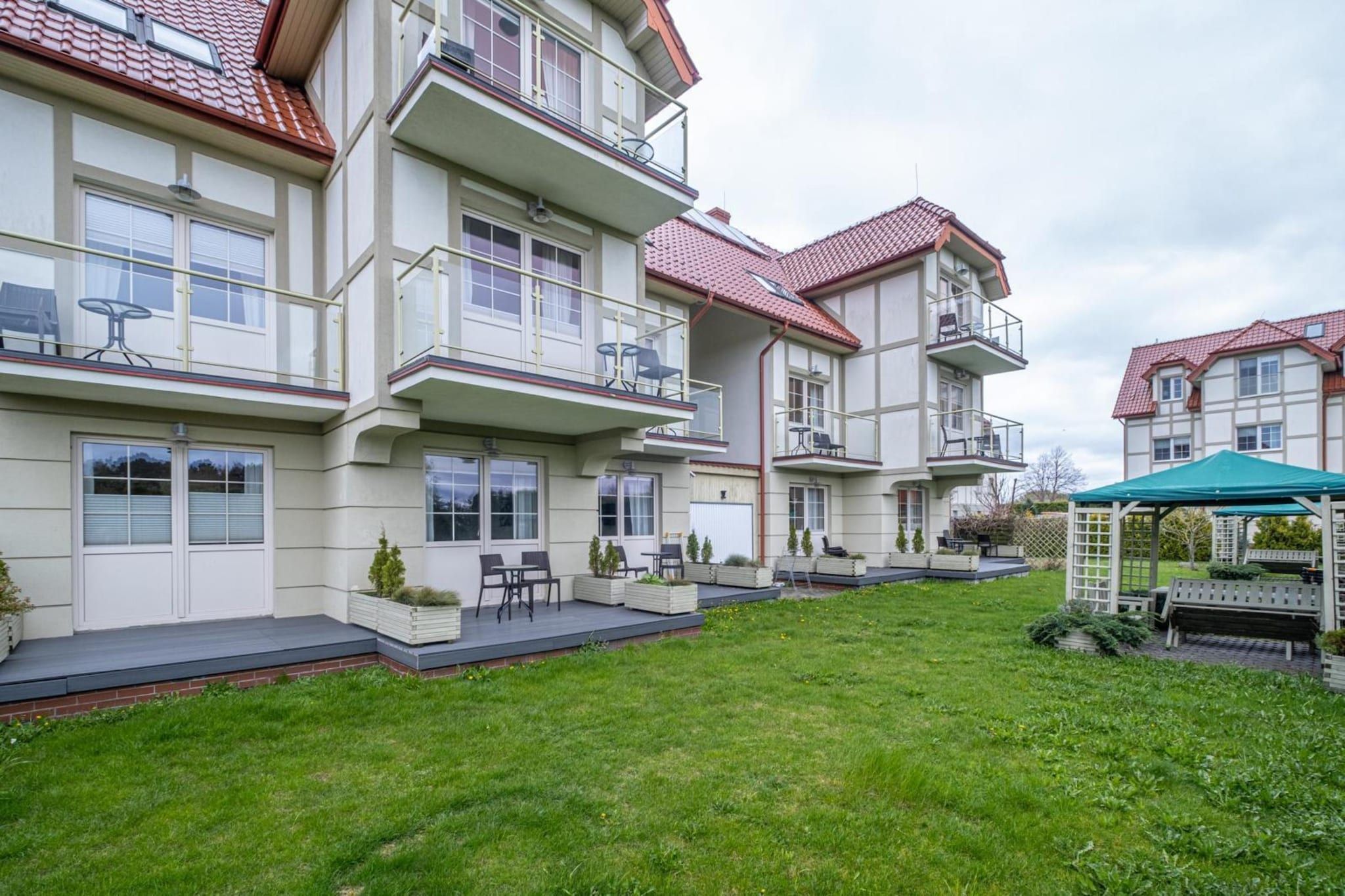 A multi-story residential building with balconies, a covered outdoor seating area, and a well-maintained lawn.