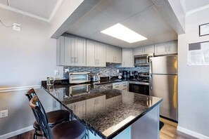 A modern kitchen with a central island, stainless steel appliances, and light-colored cabinetry. - Newly Renovated Condo Steps from the Beach with AC, WiFi & Shared Pool (Ocean City)
