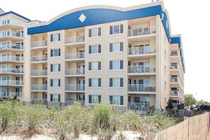 A multi-story hotel with balconies, a blue accent wall, and a sandy foreground. - Newly Renovated Condo Steps from the Beach with AC, WiFi & Shared Pool (Ocean City)