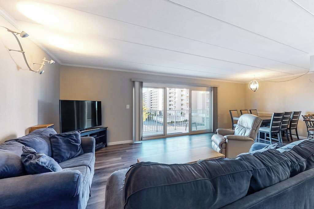 A modern living room with a sofa, TV, dining area, and large sliding glass doors to a balcony.