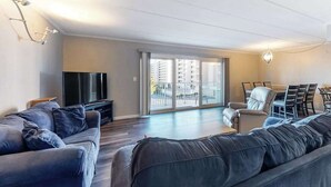 Ein modernes Wohnzimmer mit einer Couch, Fernseher, Essbereich und großen Schiebeglasfenstern zum Balkon.