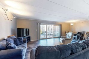 A modern living room with a sofa, TV, dining area, and large sliding glass doors to a balcony. - Newly Renovated Condo Steps from the Beach with AC, WiFi & Shared Pool (Ocean City)