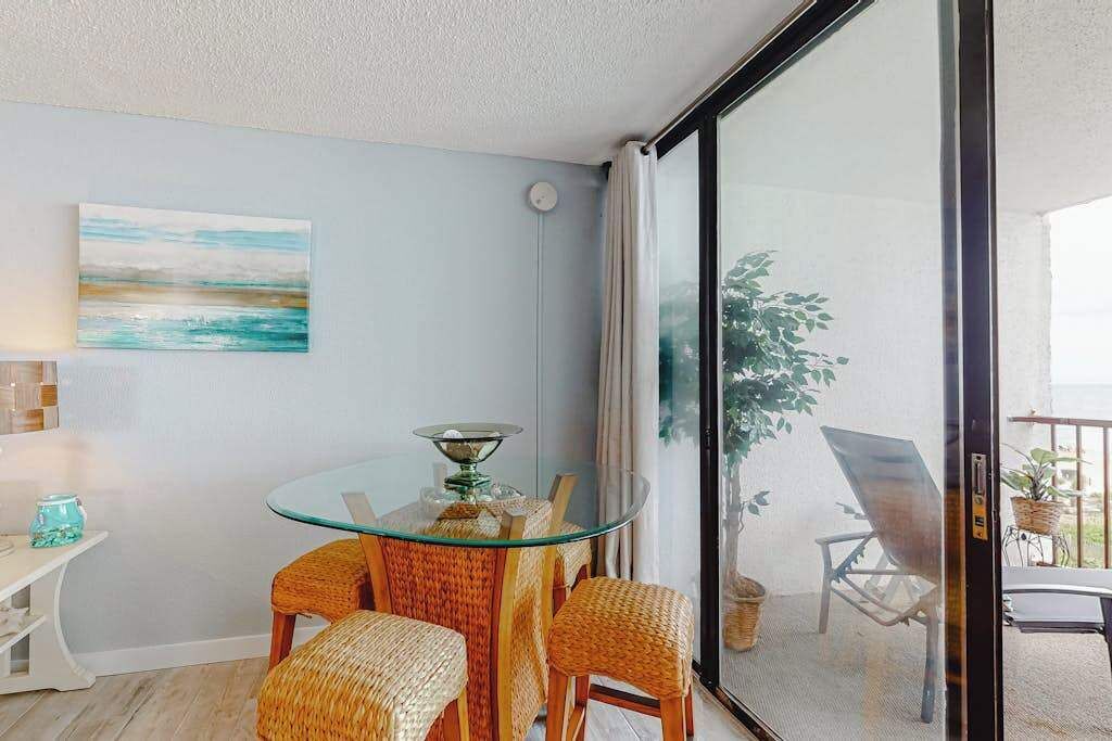 A room with a glass table, wicker chairs, a painting, and a view through a sliding glass door.