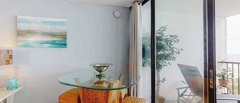 A room with a glass table, wicker chairs, a painting, and a view through a sliding glass door.