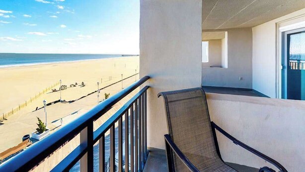 Een balkon met uitzicht op het strand, een stoel en een deur.