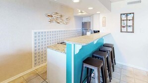 Een keuken met een bar, krukken, een koelkast en een decoratief wandobject.