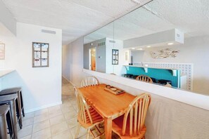 A dining area with a wooden table and chairs, a large mirror reflecting the kitchen, and a bulletin board on the wall. - Polynesian 503 (Ocean City)