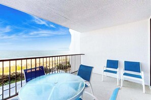 A balcony with a glass table and chairs, a view of the beach, and a white wall. - Newly Renovated, Oceanfront Condo with Balcony, Great View, AC & Shared Pool (Ocean City)