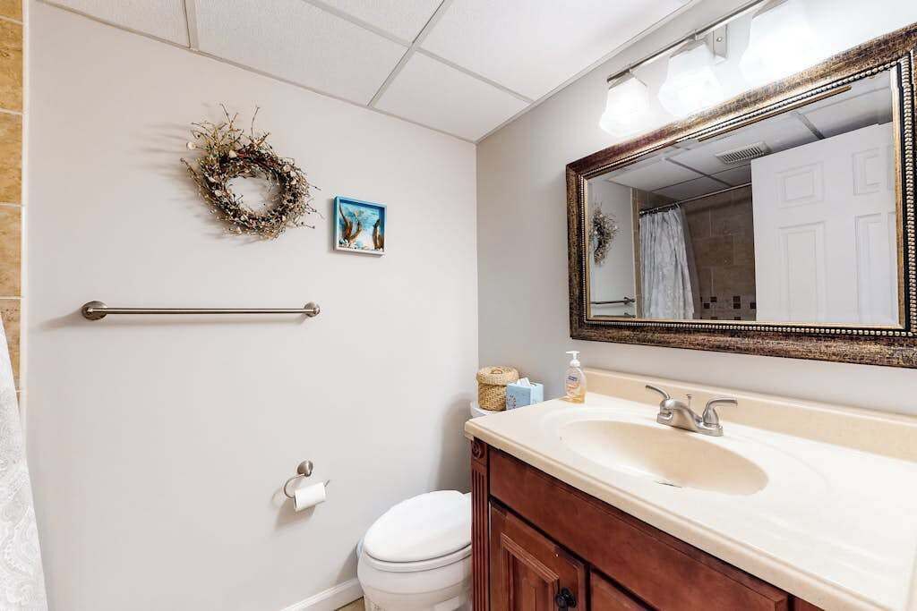Ein Badezimmer mit Toilette, Waschtisch mit Spiegel, Handtuchhalter und Toilettenpapierhalter an der Wand.