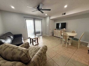A living room with a sofa, a dining table with chairs, a ceiling fan, and a television on the wall. - Outrigger 205 (Ocean City)
