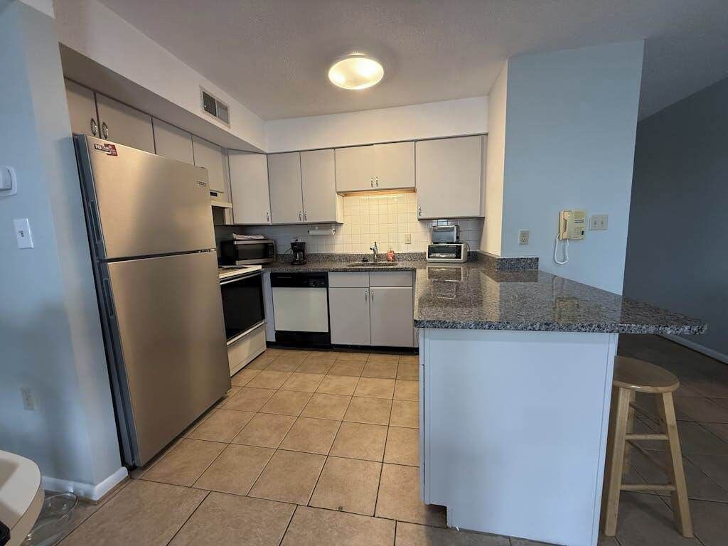 Una cocina moderna con armarios blancos, un refrigerador de acero inoxidable, horno empotrado y encimera de granito.